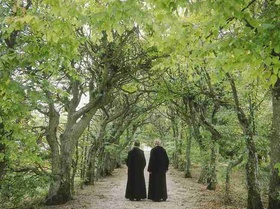 Zwei Moenche gehen durch Allee eines Gartens