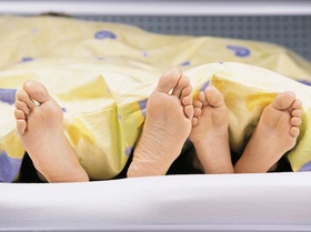 Zwei Paar Füße unter Bettdecke